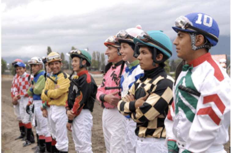 10 jockeys standing on a race track smiling at the camera before a race